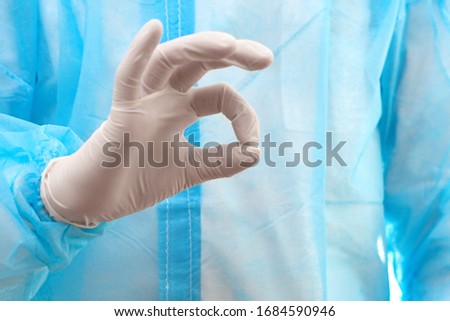 Medical worker shows gesture ok. White latex gloves, blue disposable bathrobe.