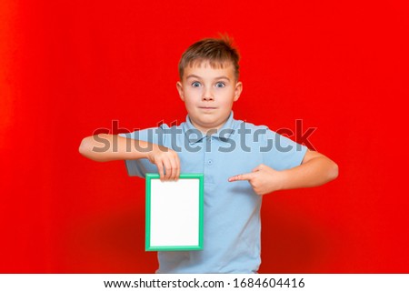 Horizontal portrait of caucasian teenage boy holding and pointing finger at empty small placard in frame for copyspace text isolated over bright red background.Copy space mock up.
