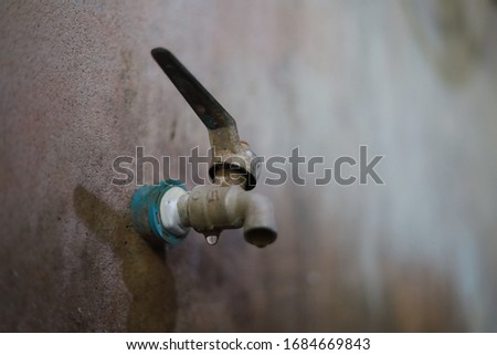 Old faucets on the wall, plastered in the bathroom, have stains and water seepage all the time. The pipe is wrapped with white tape.