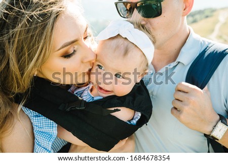 Carrying a baby. Young mother with her daughter in sling. Portrait of happy family. Mom, dad and girl walk in mountains in nature. Spending time together outdoors. The concept of summer holiday.