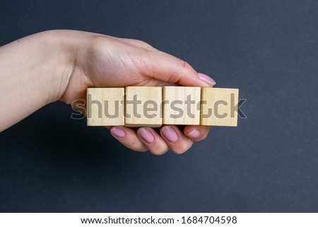 Hand holds 4 wooden cubes on a black background, space for text.