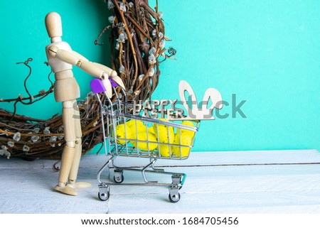 The Easter concept. Figure of a wooden man with a basket filled with eggs. In the background is a wooden rabbit and a sign of a Happy Easter and a wreath.