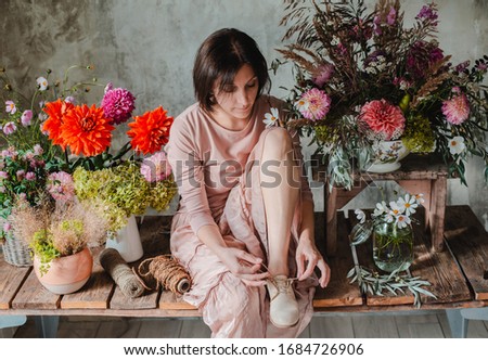Female professional florist sitting on a wooden table with a composition of wildflowers. Flower shop. Background, concrete, gray wall. Concept inspiration, floral, greetings, spring, ornament flowers.