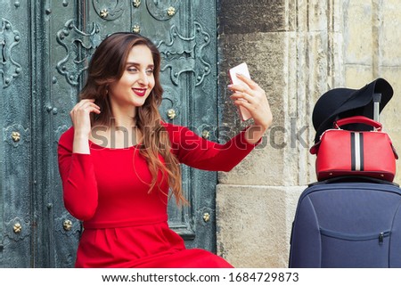 Travel woman in black hat with suitcase makes selfie near black old door.