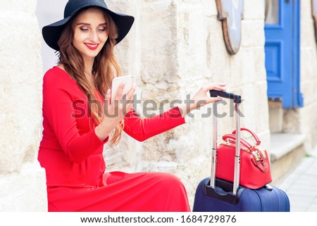 Travel woman in black hat with suitcase makes selfie at city street.