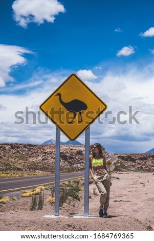 Woman standing near highway under road sign ostrich