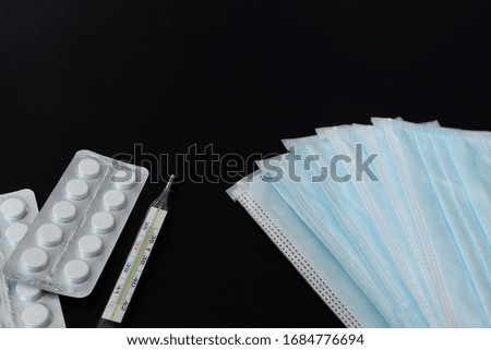 A tablets and thermometer, protective masks against the virus on a black background