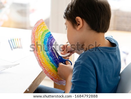  Kid is isolation using scissors cutting paper in rainbow shape on white background, Children activities at home while school off.Stay at home Social media campaign for coronavirus prevention concept