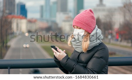 Casual Woman in Surgical Face Mask Puts on Medical Gloves and Uses Mobile App on Smartphone in City Street. COVID-19 Coronavirus Pandemic Outbreak. Picture with Copy Space