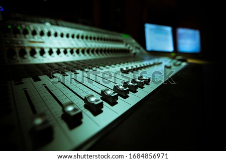 faders of a mixing panel in a sound studio with two monitors in the background