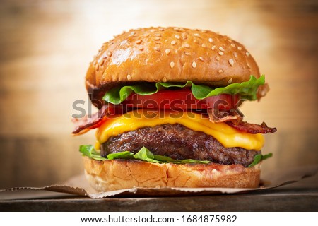 burger with cheese, bacon, salad and vegetables on a wooden  board