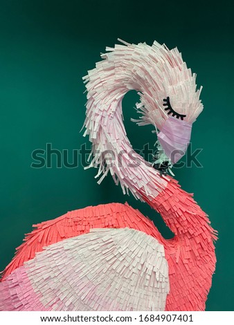 masked pink flamingo pinyatta green background. coronavirus infection protection. covid19