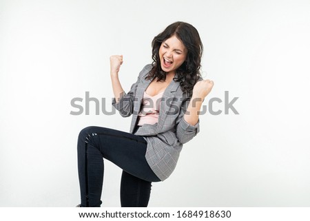 joyful brunette girl in a classic gray jacket rejoices victory on a white background