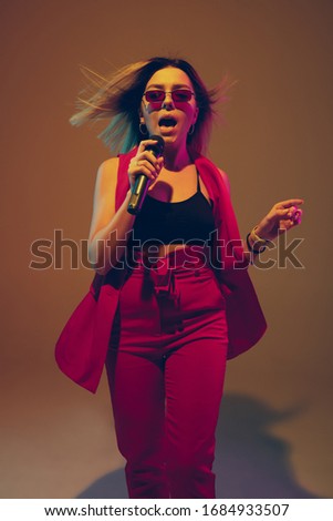 Young caucasian musician, performer singing on gradient background in neon light. Concept of music, hobby, festival. Joyful woman party host, DJ, singer, band's front artist. Colorful portrait.