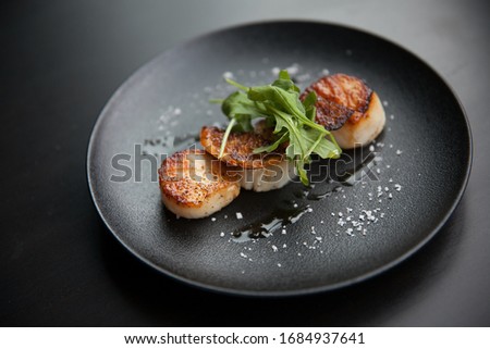 3 scallops in a black dish Royalty-Free Stock Photo #1684937641