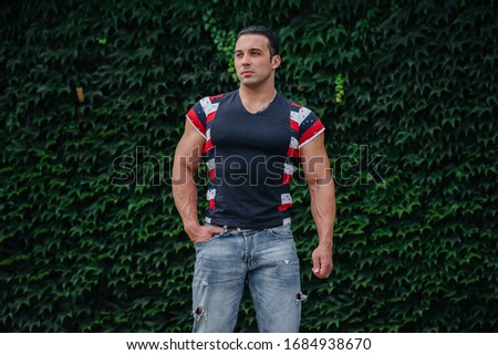 A sporty guy is sitting near a green wall of plants. Ecology