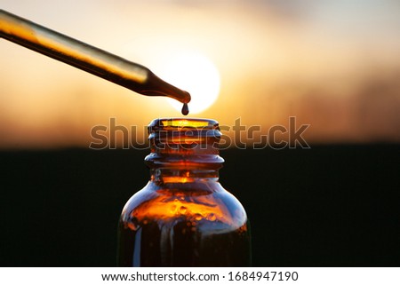 Pipette dropper of aromatherapy essence over brown glass bottle. Dropper and Brown Glass Bottle - sunset Royalty-Free Stock Photo #1684947190