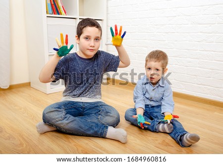 Two beautiful brothers with painted fingers sit on the floor in a white room
