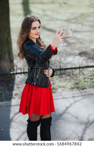 A cute young woman takes a selfie in the park. There is spring weather. The day is clear.