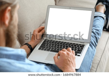 Young male tech user relaxing on sofa holding laptop computer mock up blank white screen. Man using modern notebook surfing internet, read news, distance online study work concept. Over shoulder view Royalty-Free Stock Photo #1684967884