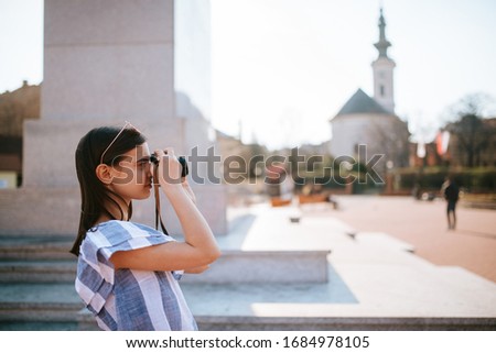 
A young caucasian beautiful girl is taking a photo with a camera next to the monument