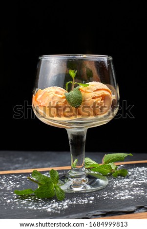 Pumpkin ice cream in a glass goblet, on a black background with a wooden board