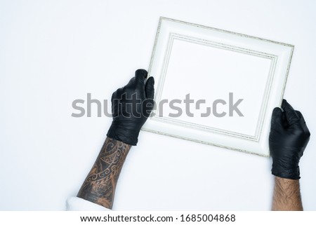 A man hand with black gloves holding a empty(blank) white photo frame isolated on white background.