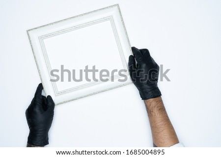 A man hand with black gloves holding a empty(blank) white photo frame isolated on white background.