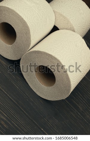 Three rolls of white toilet paper on wooden background with space for text. Deficit means of hygiene during coronavirus