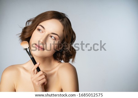 Joyful mood. Cheerful girl keeping smile on her face while holding brush for face contouring