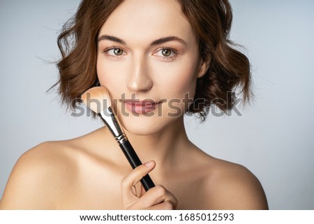 Makeup lesson. Cute brunette girl keeping smile on her face while looking straight at camera