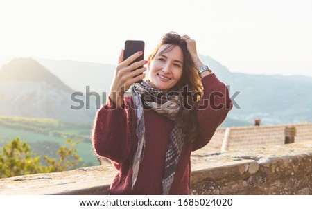 Young smiling woman making selfie on her smartphone over Tuscany mountain landsape