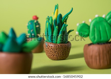 Handmade plasticine green cactuses and succulents in a pots on a color paper background.