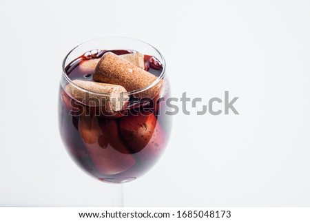 On a white background a glass with corks filled with red wine