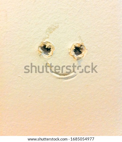 A picture frame and drywall screw anchors form a happy face in the wall. An encouraging nudge for a do it yourself carpenter or home decorator.