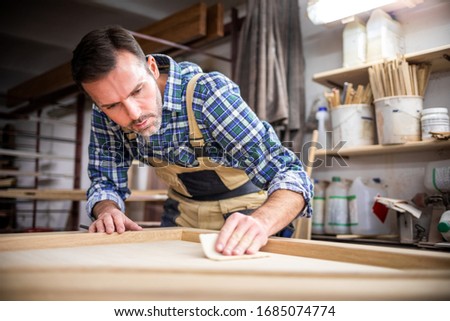Professional carpenter polishing wood using abrasive paper in carpentry workshop Royalty-Free Stock Photo #1685074774