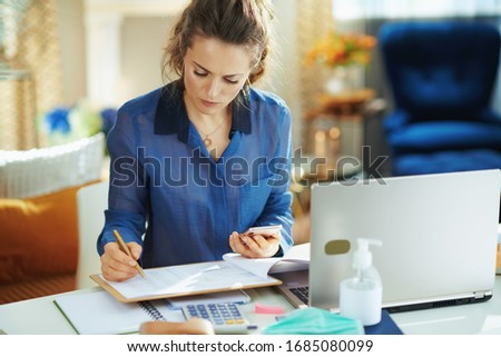 trendy middle age woman in blue blouse in the modern house in sunny day working in temporary home office during the coronavirus epidemic. Royalty-Free Stock Photo #1685080099