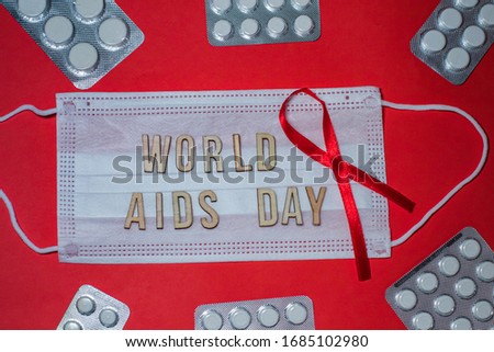 WORLD AIDS DAY is wording on protective medical mask. red ribbon and pills in blister on red background