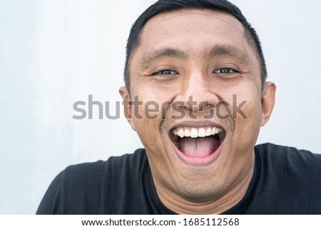 A closeup portrait of a face of an Asian Indonesian male model who smiles with his mouth wide open. he looks happy. Picture is on white background