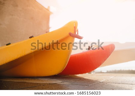Yellow plastic kayak boats stand in parking lot, sunset light. Concept trip on river lake.