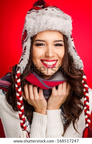 Portrait of beautiful woman in warm clothing and winter hat with bright makeup on red background. Studio portrait.