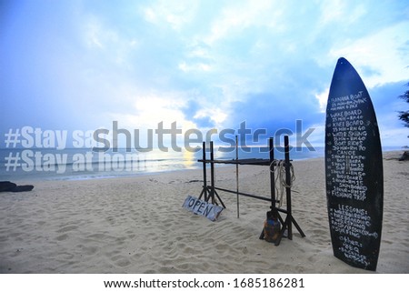 An empty beach with a signage made from  a surf board with message written stay safe.  A stay safe message due to virus concept