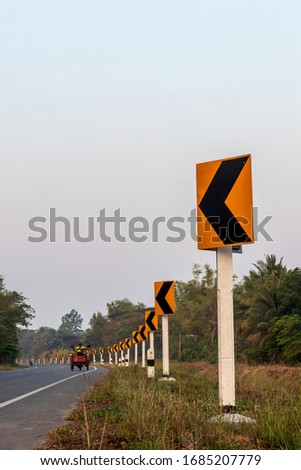 Low angle view, curvy road signs beside the Thai rural road, in which a tricycle is passing by during the day.