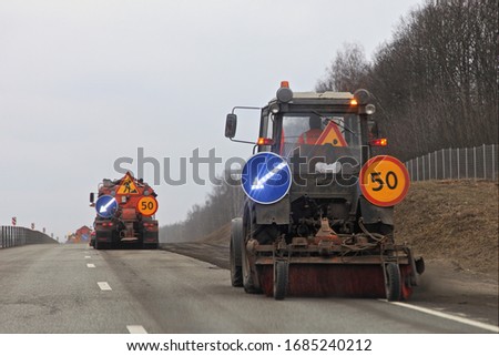 Road cleaning in Russia, asphalt sweeper tractor cleans spring roadside on trees background, municipal highway maintenance service mechanisation