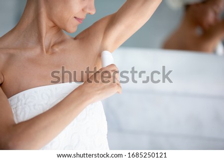 Happy 30s beautiful woman applies antiperspirant stick after shower in morning close up image. Using treatment for bodycare skincare, to reduce sweating, underarm wetness and control body odor concept