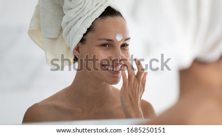 Woman reflected in mirror after morning shower with towel on head applies day facial cream close up, prevent first wrinkles, caring about skin use moisturizer creme, beauty treatment, skincare concept Royalty-Free Stock Photo #1685250151