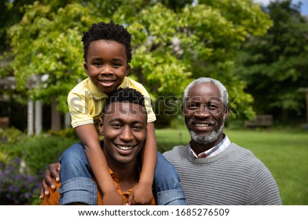 Portrait of a smiling African American grandfather in the garden with his adult son and his grandson on piggyback. Family enjoying time at home, lifestyle concept