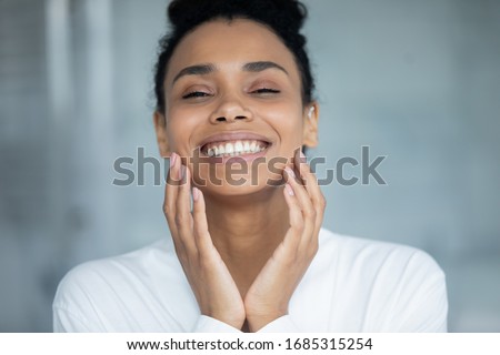 Beautiful african woman touch face enjoy ideal flawless fresh smooth facial skin close up portrait. Laser skin resurfacing, glycolic acid peel, anti-ageing skincare procedures and cosmetics ad concept Royalty-Free Stock Photo #1685315254