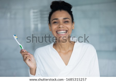 Head shot portrait gorgeous happy African woman wear bathrobe smiling looking at camera holding in hand toothbrush with soft bristle for sensitive teeth. Personal self-care and oral hygiene concept Royalty-Free Stock Photo #1685315257