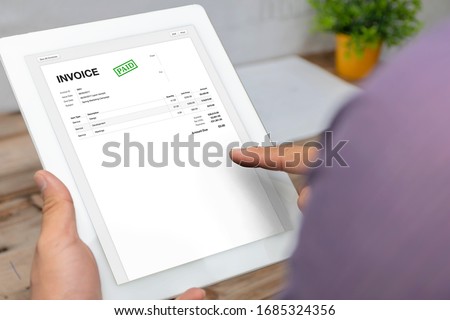 Close-up of businessman's hands working on invoice on tablet calculating Tax at desk in office